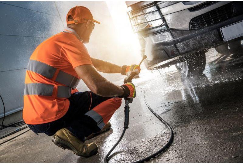 Man using power washer to clean bus